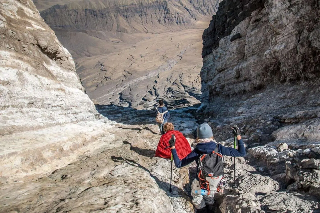 Hikers ascending the volcanic slopes of Mount Ol Doinyo Lengai with a dramatic sky backdrop.