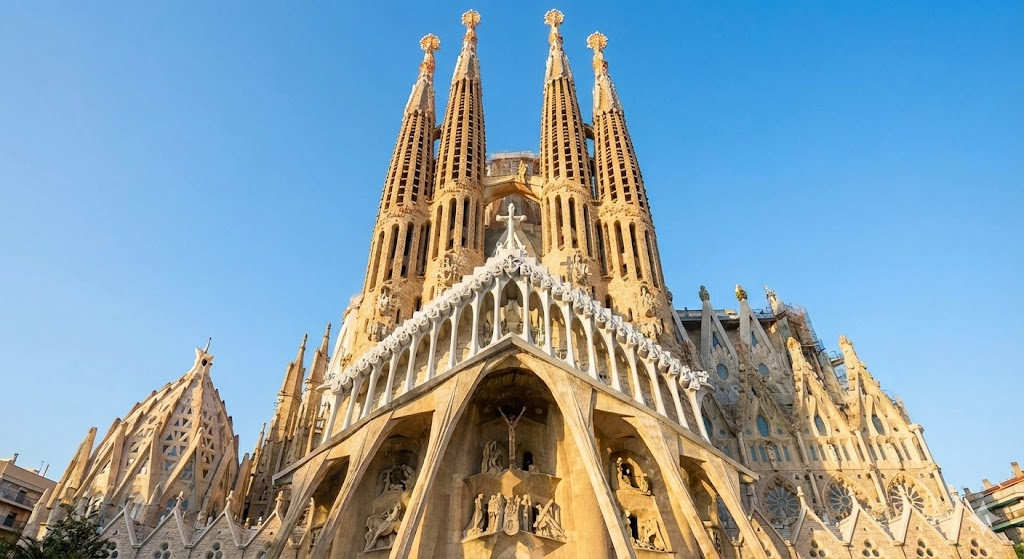 A detailed architectural view of the Nativity Facade and towering spires of the Sagrada Familia basilica against a clear blue sky in Barcelona.